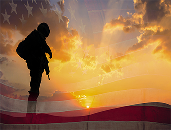 A picture of a soldier as the sun sets with the United States Flag in the background.